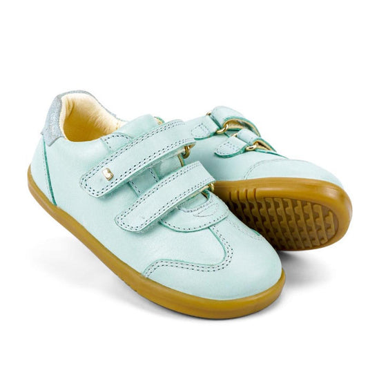 The Bobux Kids IWalk IW Sprite Sneaker in Mist Blue is a pair of light blue unisex shoes with double strap closures and tan rubber soles, displayed on a white background.