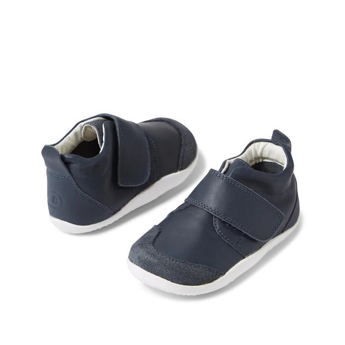 The Bobux XP Explorer Rover First Walker Boot Navy 502601 features soft material, flexible white soles, hook-and-loop Velcro straps, and is shown in navy blue on a white background.