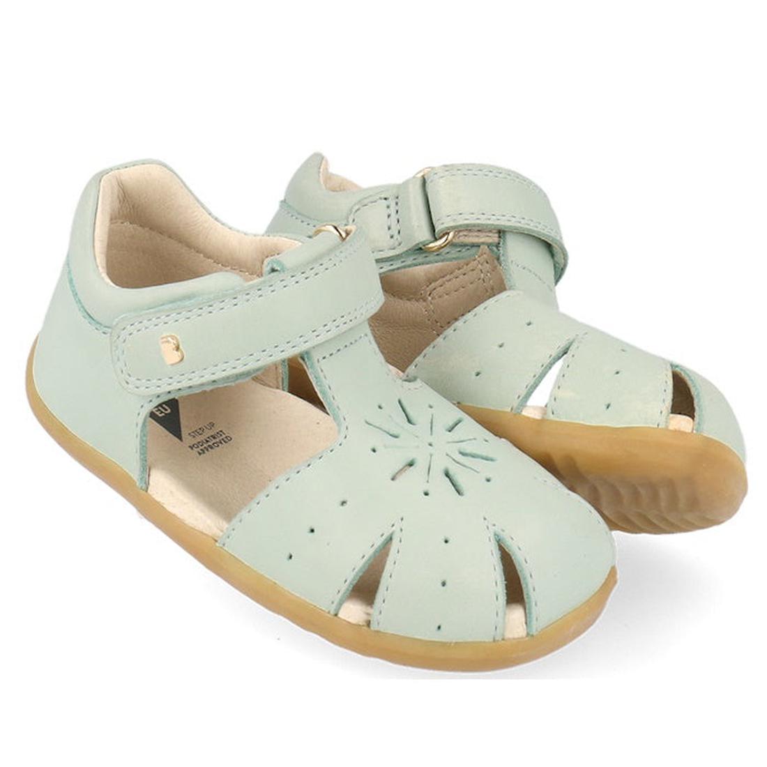 Bobux Step Ups Compass Mist Aqua 734905 Toddler Girls Sandals feature light blue leather, tan rubber soles, closed toes with cut-out details, adjustable Velcro ankle straps, and a soft cushioned interior for comfort.