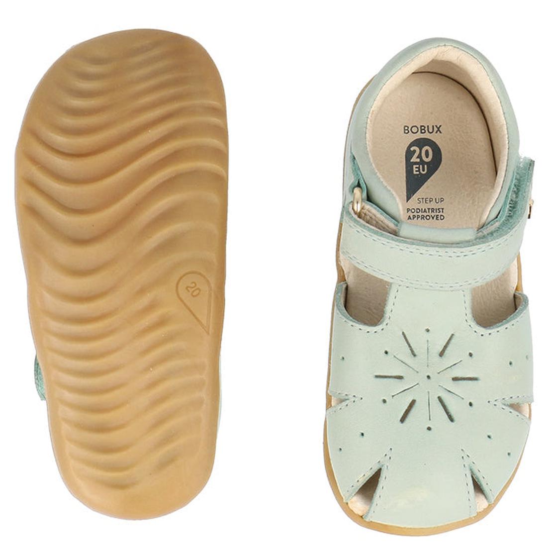 The Bobux Step Ups Compass Mist Aqua 734905 Toddler Girls Sandal features light blue closed toes, tan rubber soles, a textured sole bottom, and a cutout starburst design—perfect as first walker shoes., 9420075708594, 9420075708600, 9420075708617, 94200757, 9420075708624