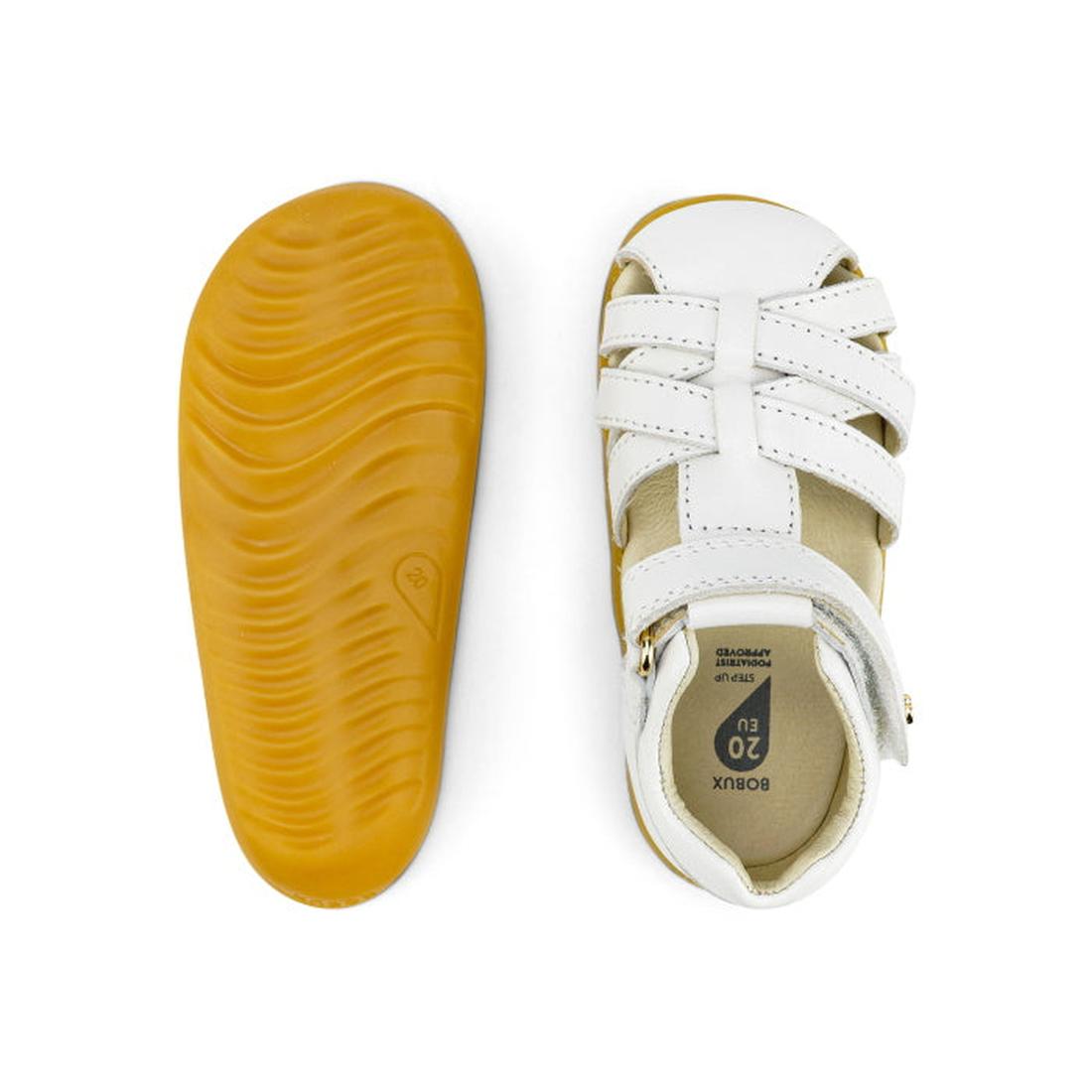 The Bobux Step Ups Cross Jump White 731106 Closed Toe Sandal features white leather straps, a tan rubber sole, and a kids-first walker design; one sandal is shown from the top while the other displays its textured sole., 9420062083901, 9420062083918, 9420