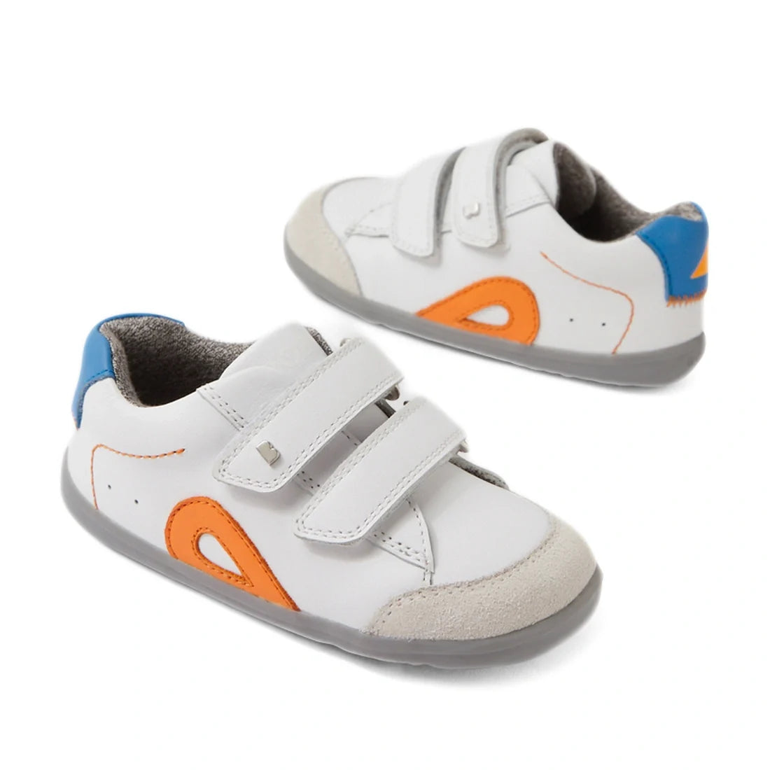 A pair of Bobux SU Step Up Blaze Leather Toddlers Sneaker in white and orange, featuring gray soles, blue and orange accents, suede toe caps, and two velcro straps on each shoe—perfect as first walking sneakers.