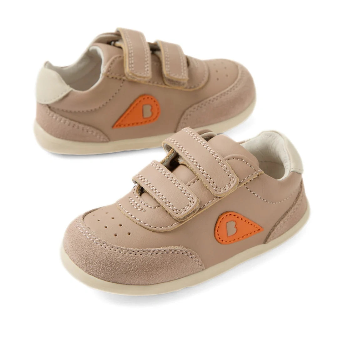 Two Bobux Step Up SU Champ Sneaker First Walker shoes in warm taupe are displayed on a white background. These toddler sneakers feature velcro straps, cream soles, an orange patch with a “B” on the side, and suede accents for added style and durability.