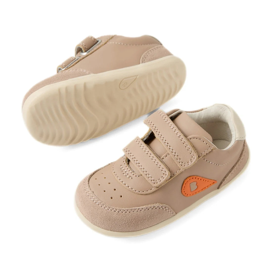 A pair of Bobux Step Up SU Champ Sneaker First Walker shoes in warm taupe for toddlers, featuring hook and loop straps, rubber soles, and an orange teardrop-shaped detail on the side, shown from the side and bottom views., 9420074861894, 9420074861900, 94