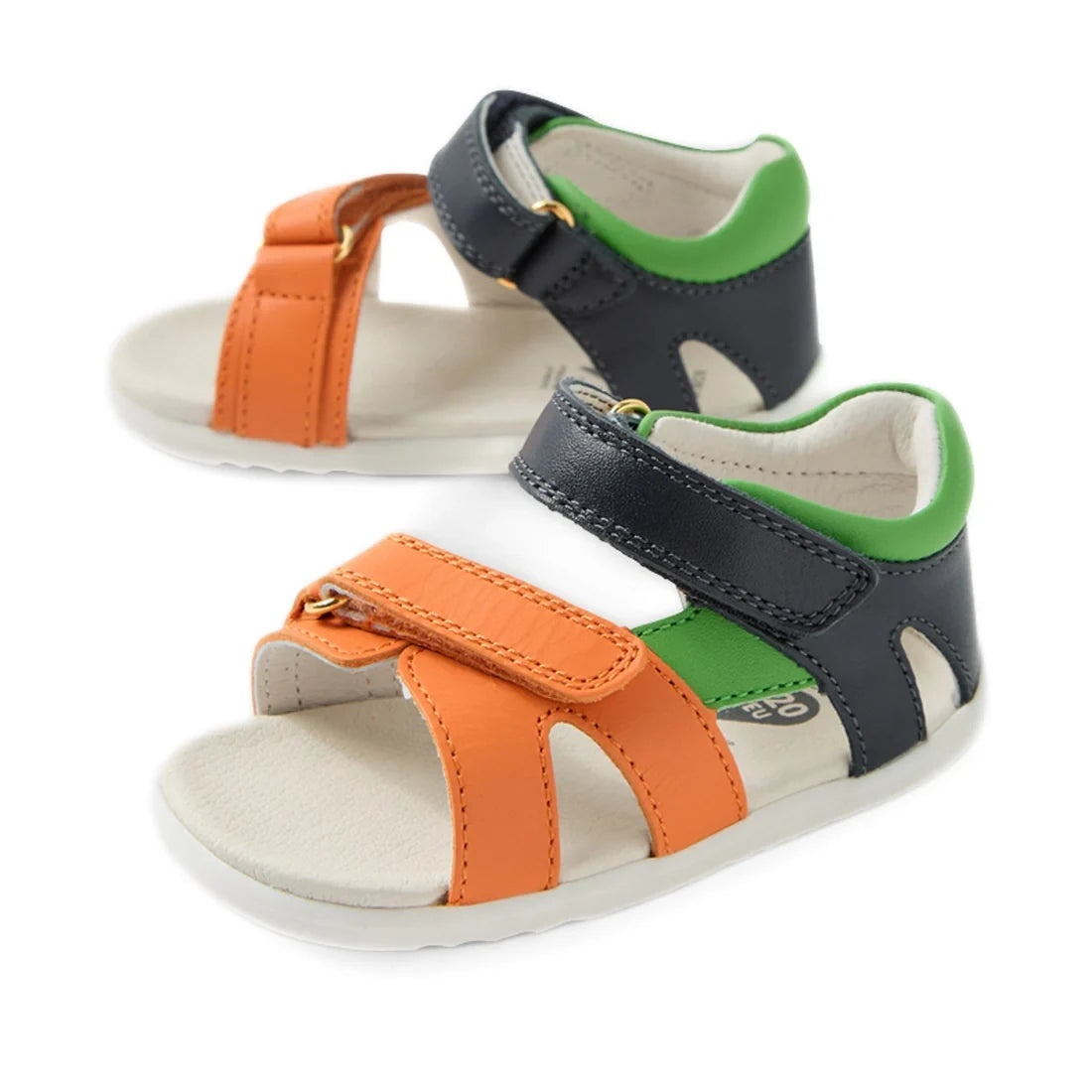 The Bobux SU Step Up Dune First Walker Open Toe Sandal Navy is an adventure-ready sandal for toddlers, featuring orange and navy blue straps, a green inner lining, white soles, and Velcro fastenings.