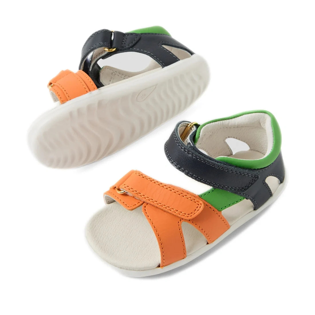 Two Bobux SU Step Up Dune First Walker Open Toe Sandal Navy shoes for toddlers, featuring adventure-ready orange, green, and navy straps, white soles with a wavy grip pattern, and convenient hook-and-loop fastenings are shown—one lying flat and the other 