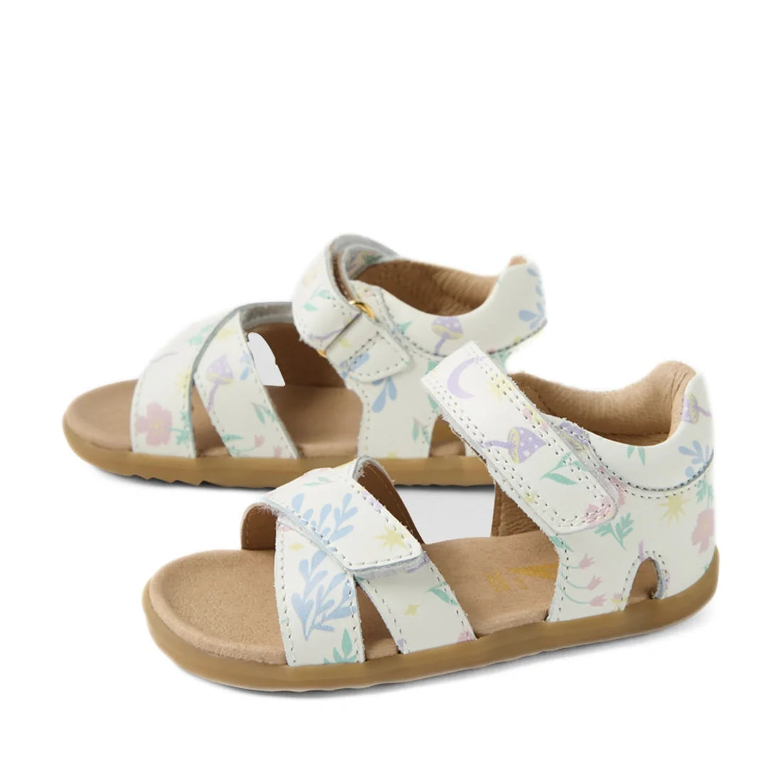 The Bobux Step Up Flora First Walker Sandal in White Floral is a pair of children’s open-toe, open-heel leather sandals featuring pastel-colored floral and plant patterns on a white background, beige soles, and adjustable straps—perfect as little ones’ fi