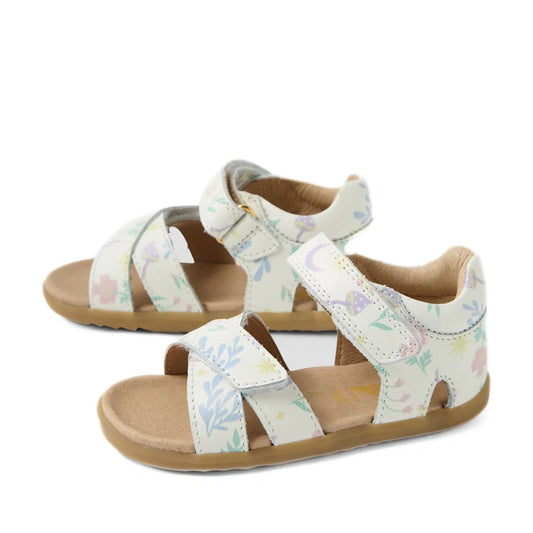 The Bobux Step Up Flora First Walker Sandal in White Floral is a pair of children’s open-toe, open-heel leather sandals featuring pastel-colored floral and plant patterns on a white background, beige soles, and adjustable straps—perfect as little ones’ fi