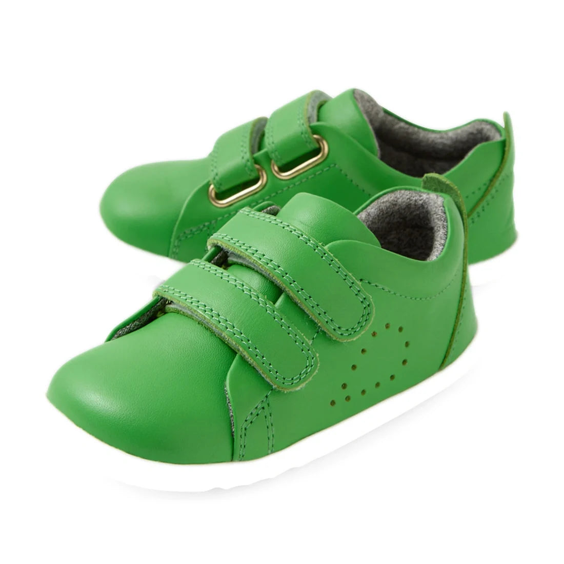 A pair of small, bright green kids’ leather sneakers—Bobux Step Up Grass Court Trainer Retro Green—with white soles, two hook-and-loop straps, and perforated side detailing, displayed on a white background.