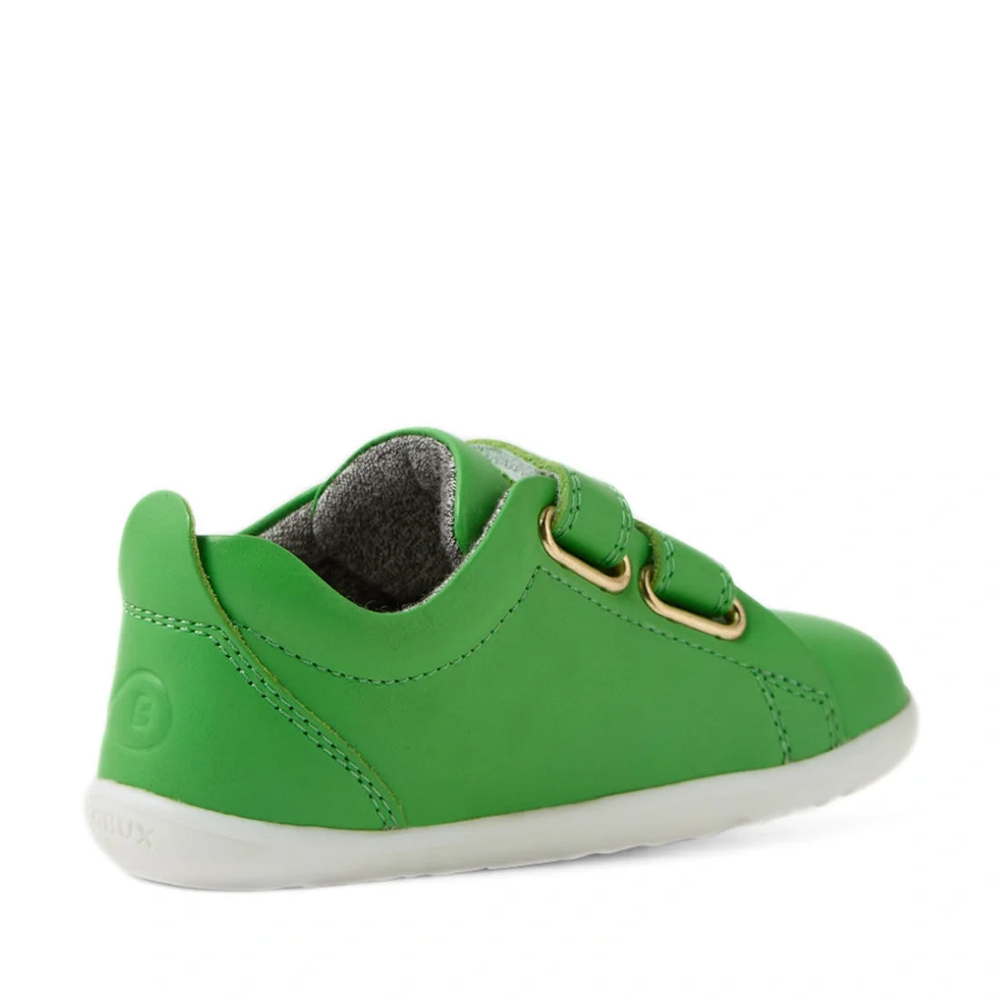 A pair of Bobux Step Up Grass Court Trainer Retro Green sneakers for kids, ideal as a first walker, is shown from the back-left side, highlighting its retro green leather upper with two velcro straps, gold eyelets, a light gray sole, and a gray inner lini