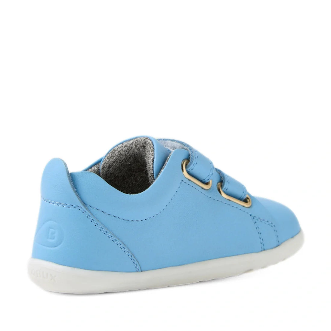 A Baltic Sea Blue Bobux Step Up Grass Court Trainer for kids, crafted in leather with two Velcro straps, gold eyelets, and a white sole, shown from the back right side against a white background—ideal for little first walkers., 9420074806604, 942007480661