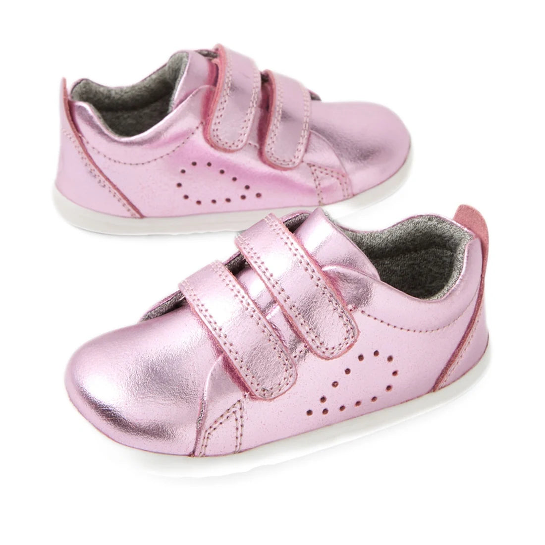 Bobux Step Up Grass Court Trainer Pink Metallic toddler shoes feature a shiny pink finish, two velcro straps, and white soles, displayed on a white background—perfect first walkers designed to support your little one’s earliest steps.