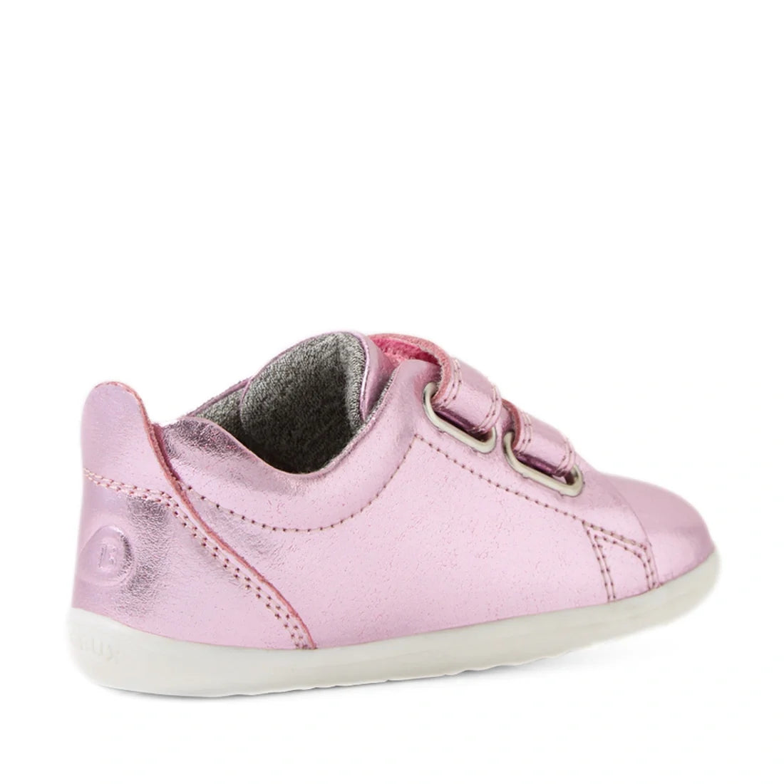 A shiny pink metallic Bobux Step Up Grass Court Trainer, featuring a white sole and two Velcro straps—ideal for first walkers—is viewed from the side and slightly behind, set against a white background., 9420074806406, 9420074806413, 9420074806420