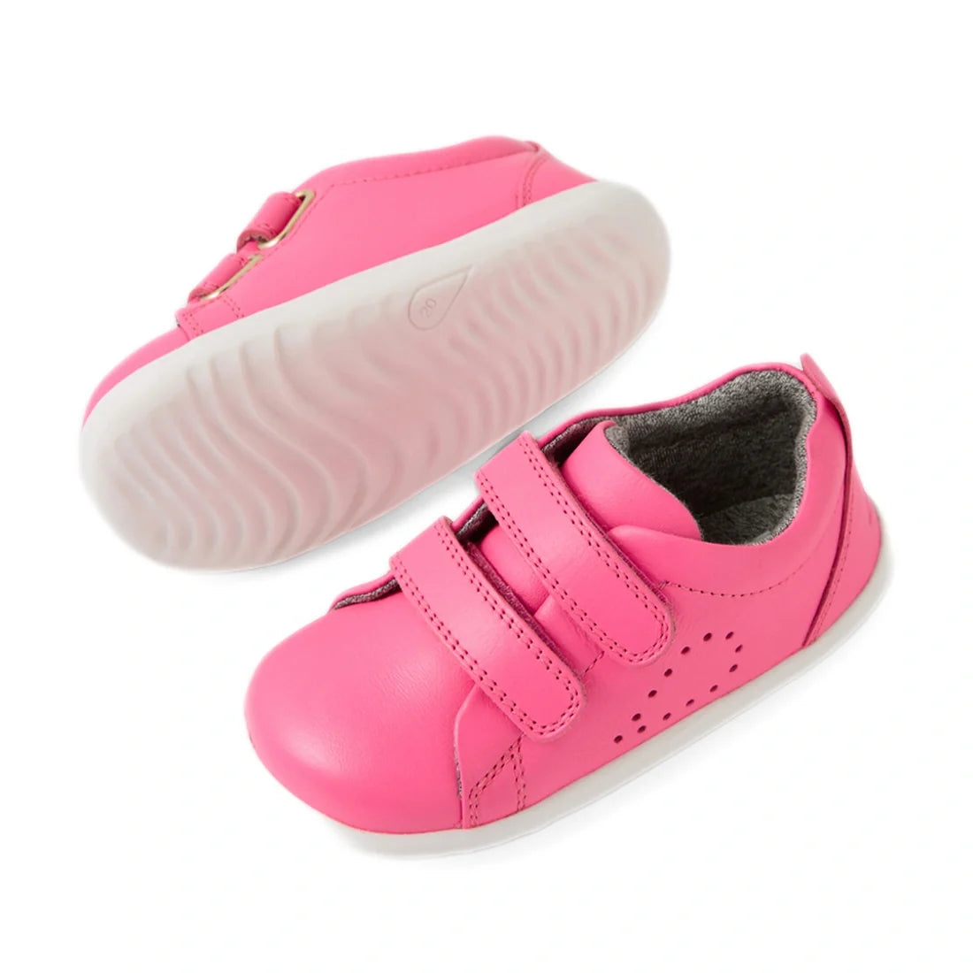 Introducing the Bobux Step Up Grass Court Trainer in Pink Lemonade: This pair of vibrant pink leather kids’ sneakers features white soles, handy Velcro straps, and a soft grey interior for comfort. One trainer is shown from the side and the other from und