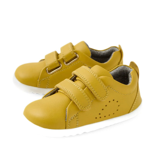A pair of Bobux Step Up Grass Court Trainer Mango Mint Yellow toddler shoes, featuring white soles and two Velcro straps, displayed on a white background.