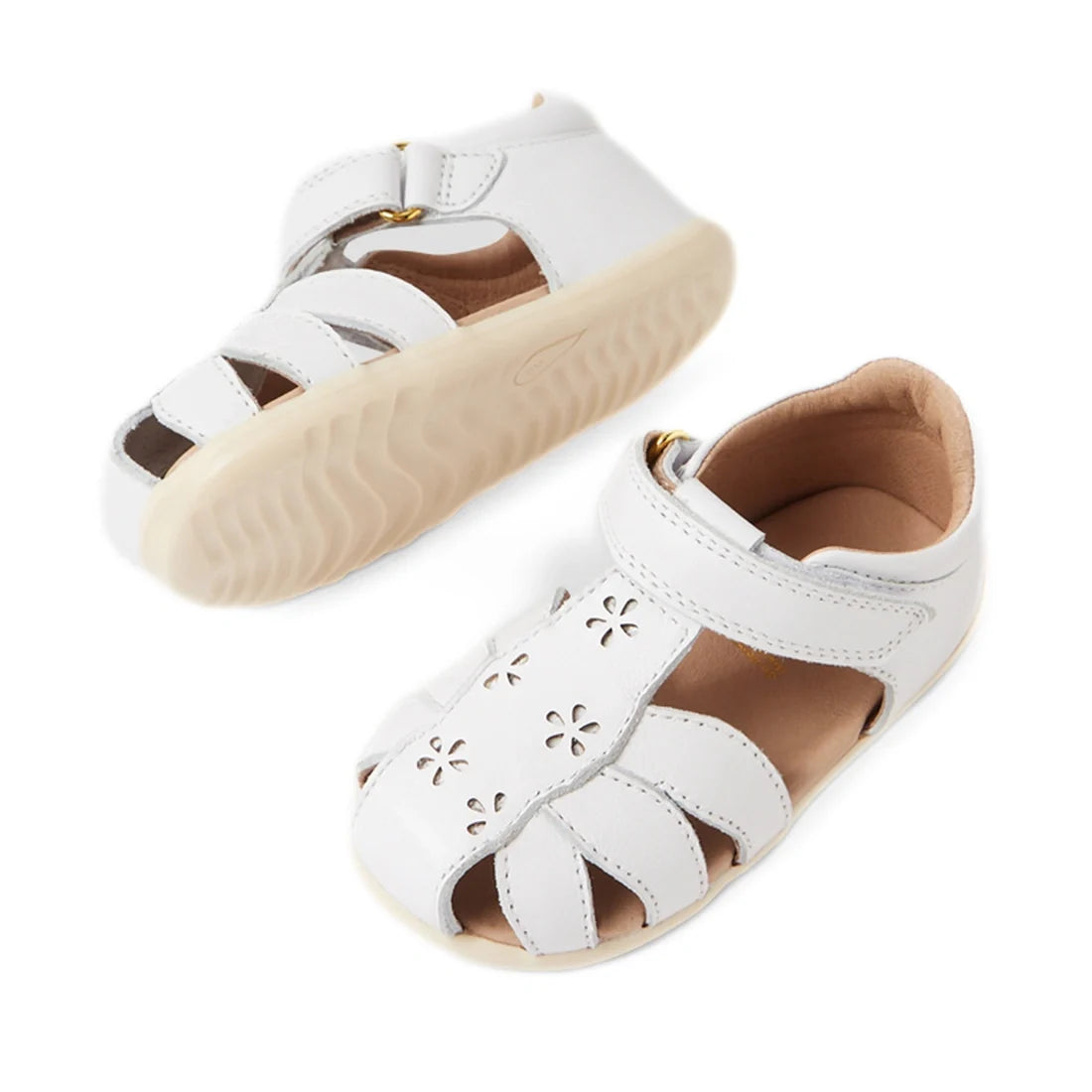 Introducing the Bobux Step Up Grass Holly First Walker Closed Toe Sandal in White—a charming pair of toddler sandals featuring cutout floral patterns, Velcro ankle straps, and beige rubber soles, making them the perfect first walking sandals for your litt