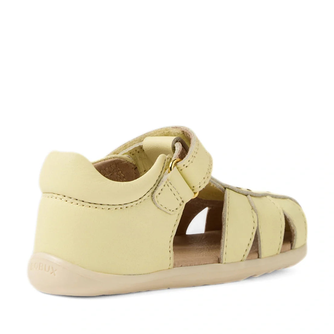 The Bobux Step Up Grass Holly First Walker Closed Toe Sandal in Wax Yellow is a light yellow sandal for toddlers, featuring a closed toe and heel, open sides, and a Velcro strap. It is designed as a first walker sandal and shown from the back left angle o