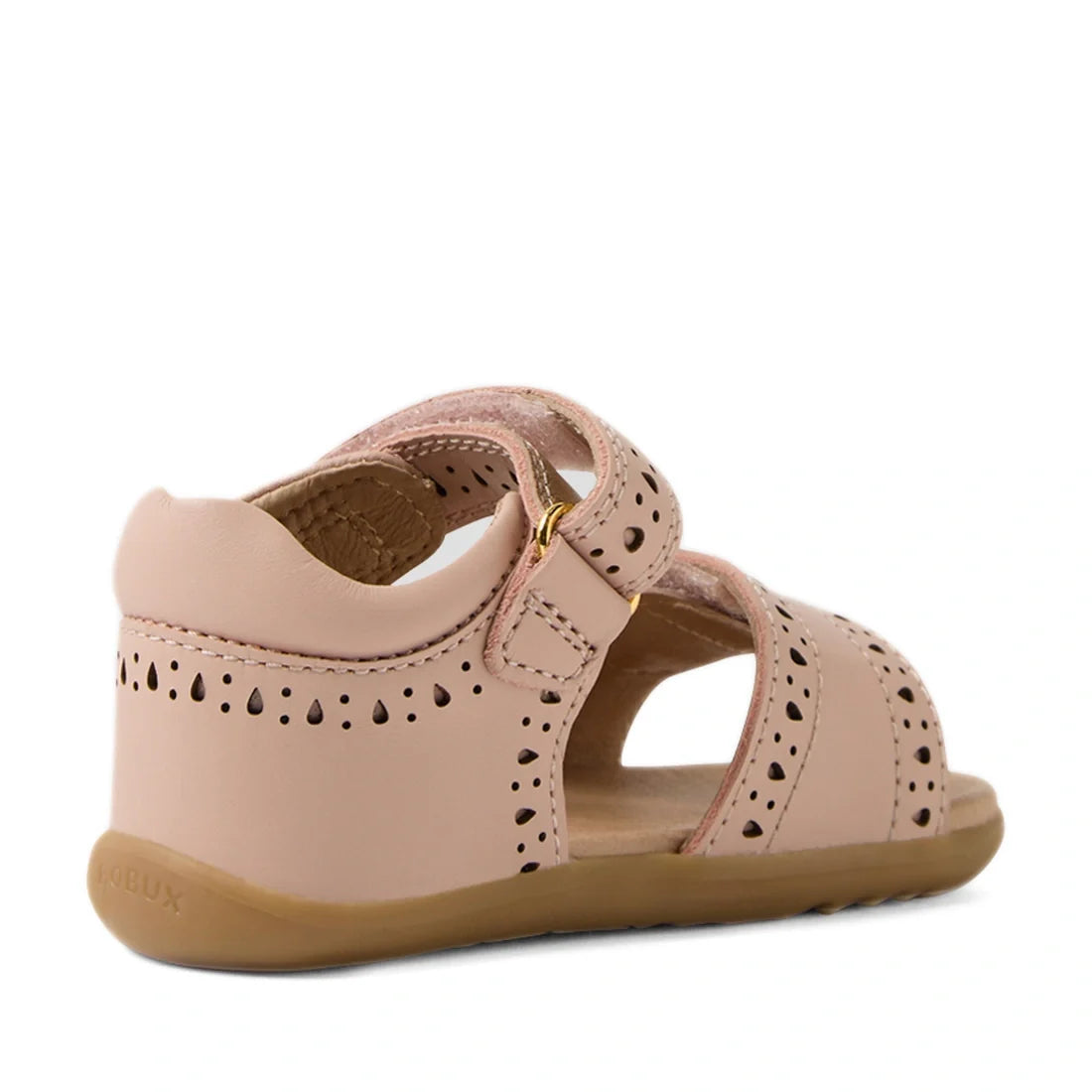 Bobux Step Up Grass Logan First Walker Sandal in Cameo Rose Pink—first walker girls’ leather sandals with decorative cutouts, a closed heel, open toe, ankle strap with gold buckle, and a flexible tan rubber sole; shown from the back left side., 9420074849