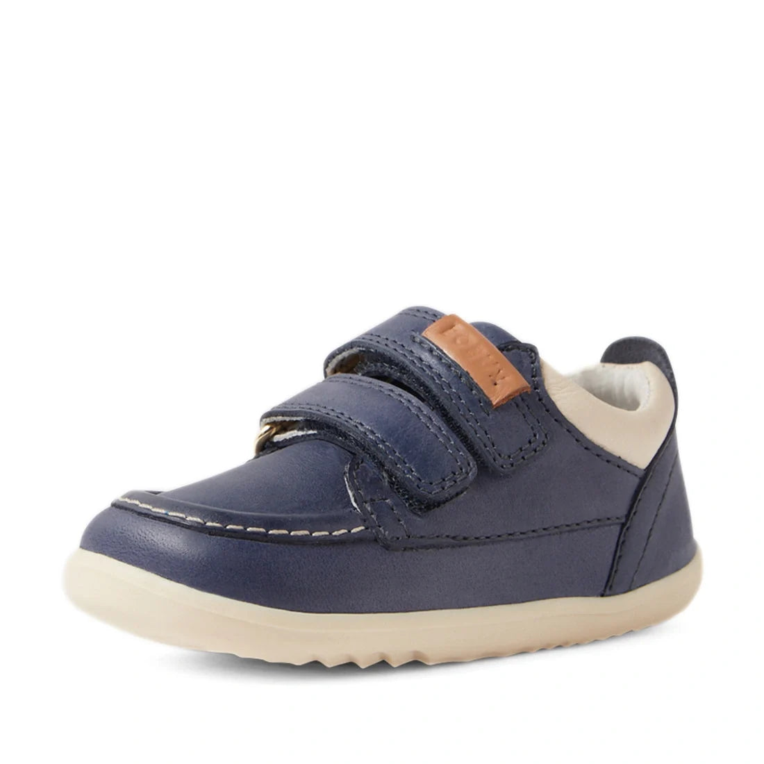 The Bobux SU Step Up Oakley Leather Toddlers Sneaker in Vintage Indigo is a small, navy blue moccasin-style boat shoe featuring two velcro straps, a beige sole, white inner lining, and a brown accent on the strap. Shown on a white background, these sneake