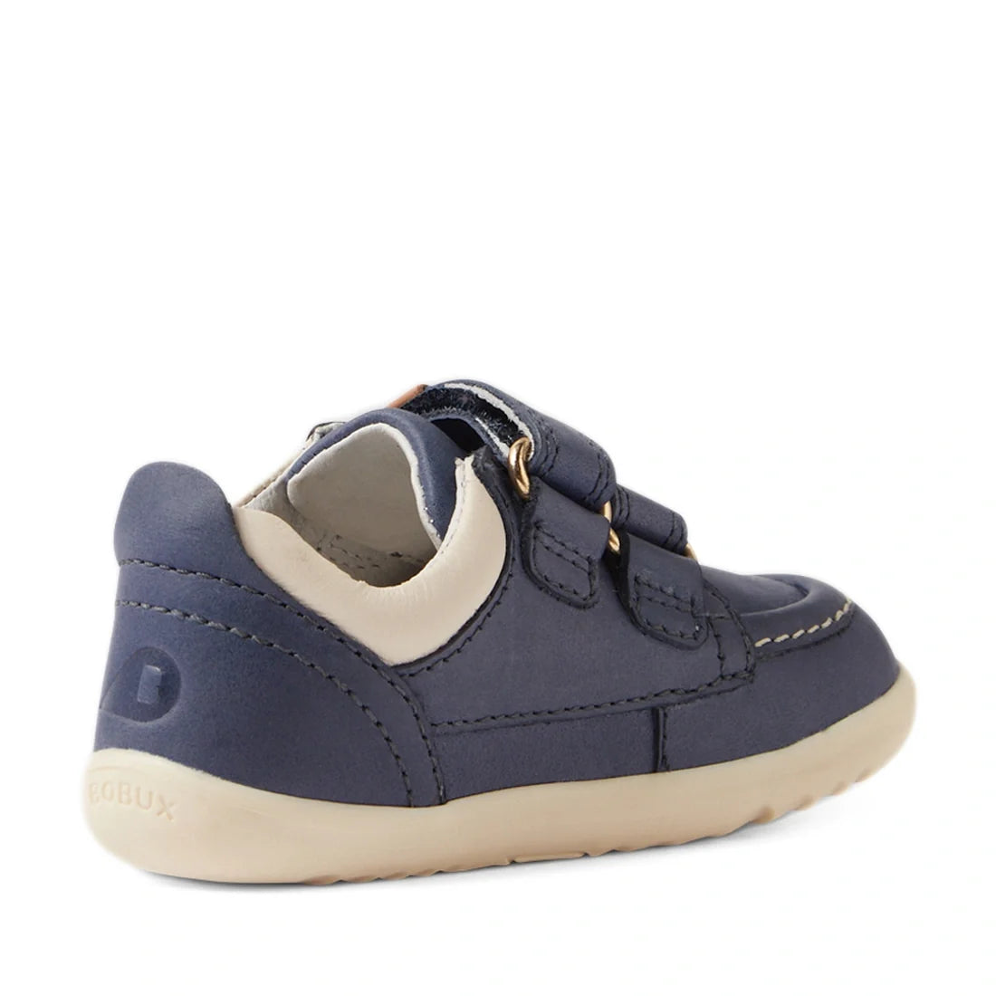 Introducing the Bobux SU Step Up Oakley Leather Toddlers Sneaker in Vintage Indigo—a navy blue toddler shoe with beige accents and a tan sole. Designed with two Velcro straps and detailed white stitching, this sneaker is shown from the back and side, maki
