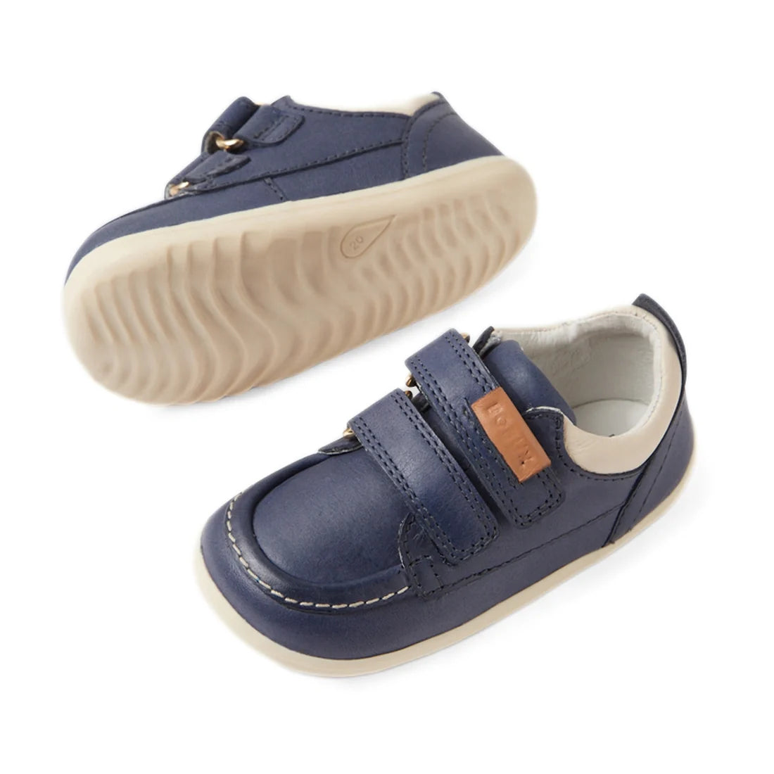 The Bobux SU Step Up Oakley Leather Toddlers Sneaker in Vintage Indigo features navy blue leather, white soles, Velcro straps, and a brown tag detail—pictured from the side and bottom on a white background., 9420074849793, 9420074849809, 9420074849816