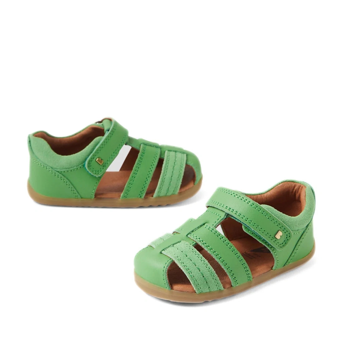 A pair of Bobux Step Up Sandal Roam Closed Toe Sandals in Retro Green, featuring small green leather uppers, brown soles, and adjustable Velcro straps—perfect for first walkers—displayed on a white background.