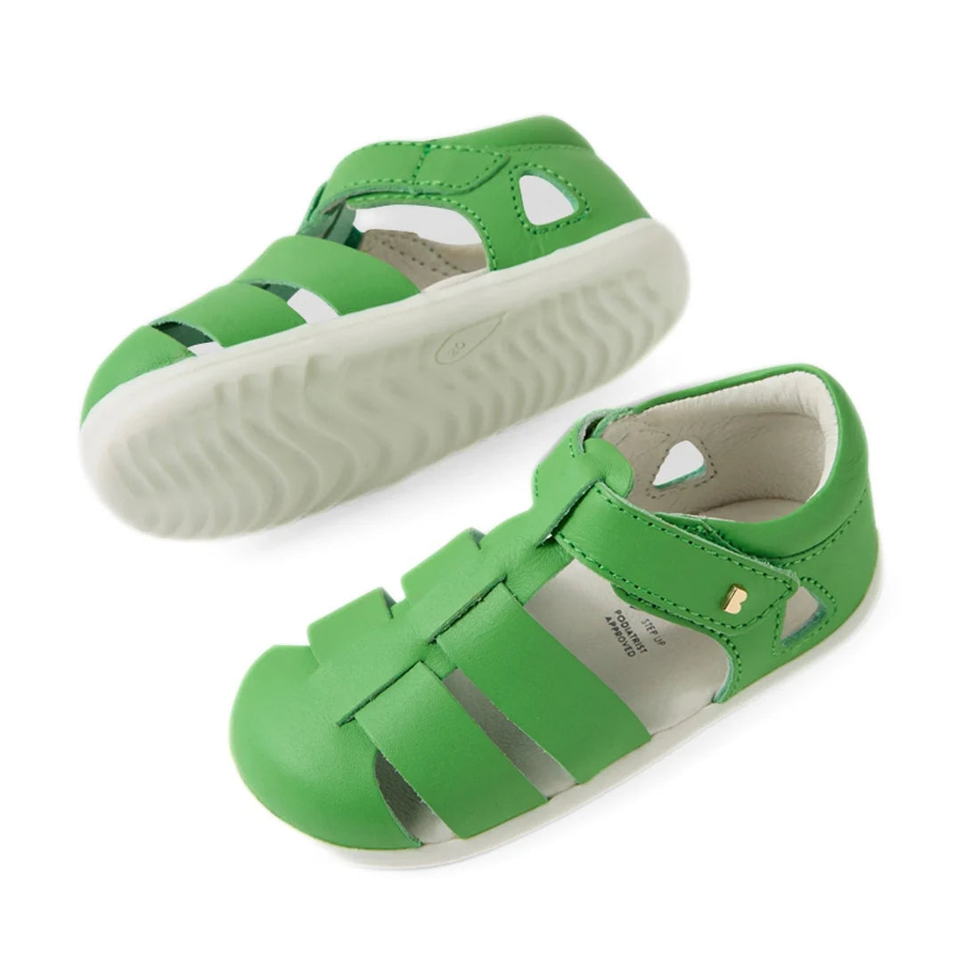 Two Bobux Step Up SU Toddlers Tidal Retro Green Closed Toe Sandals are pictured from the side and top. These water-friendly leather sandals, featuring cut-out details and a small gold button on the side, have white rubber soles. Designed for everyday adve