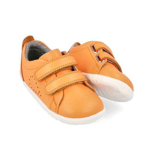 The Bobux Step Up Grass Court Trainer Apricot Crush 734209 are kids’ orange leather sneakers with white soles and double velcro straps, shown on a white background.