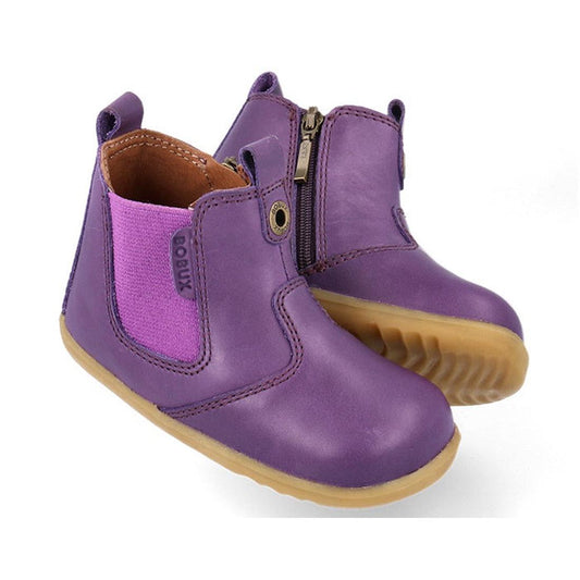 The Bobux Step Up Jodphur Boot Indigo Purple is a unisex toddler boot featuring leather in indigo purple, side zippers, stretchy panels, tan rubber soles, and brown interior lining—ideal for first walkers. A small “Bobux” tag appears by the ankle.