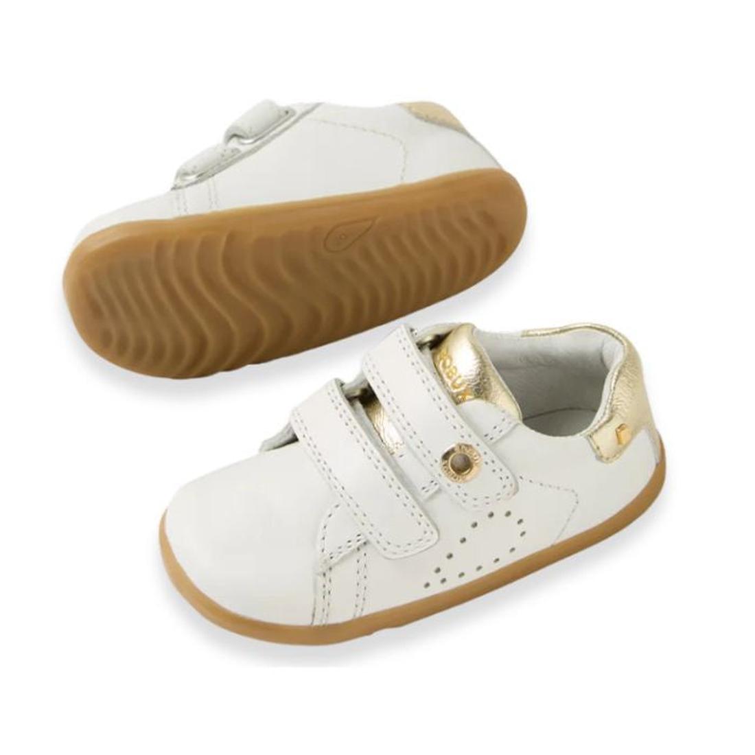 The Bobux SU Step Up Maverick Leather Toddlers Sneaker White Gold features white leather, brown rubber soles, gold accents on the heel and tongue, two adjustable straps, and decorative stitching—ideal as first walker shoes for toddlers.