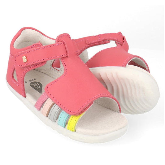 The Bobux Step Up Mirror Leather Sandal in Guava Bright Pink Rainbow (727341) features open toes, a Velcro strap, and multicolored pastel bands—perfect first walker sandals for girls—shown against a white background.