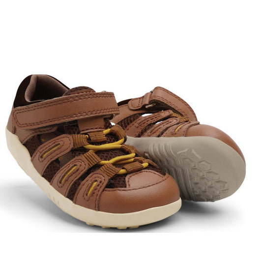 The Bobux Step Up Summit Caramel Toffee Sandal 731609 is a brown sandal for first walkers with Velcro straps, yellow elastic laces, mesh sides, water-friendly leather, and a light-colored rubber sole; one shoe is upright and one on its side.