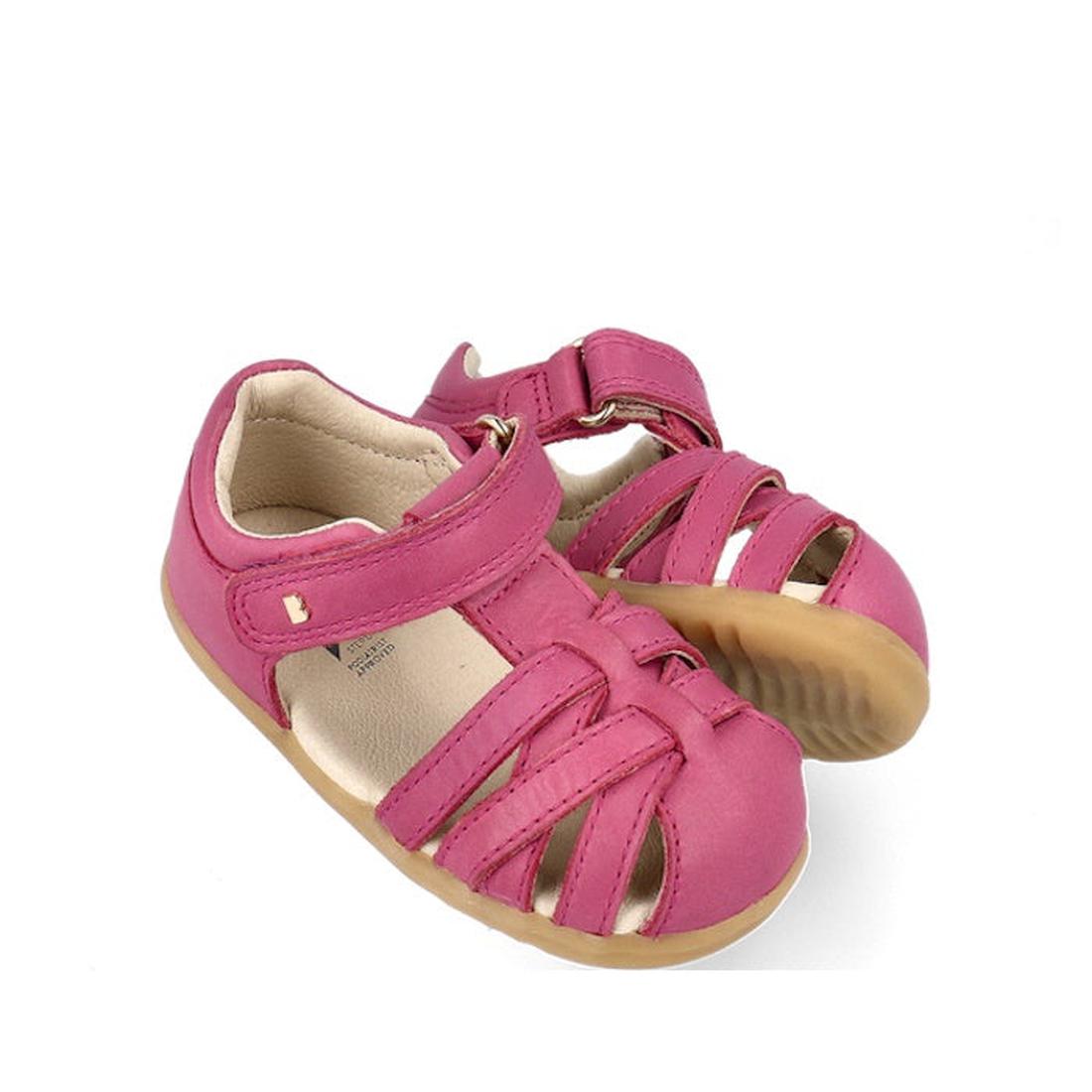The Bobux Step Ups Cross Jump Mauve Haze 731116 Closed Toe Sandal features a pink leather upper, closed toes, open sides, tan rubber soles, adjustable Velcro straps, and a cushioned lining—perfect for first walkers.