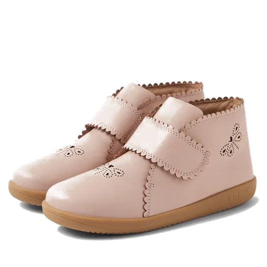 The Bobux Step Up Willow First Walker Boot in Cameo Rose Pink features scalloped edges, adjustable Velcro straps, butterfly cut-outs, and light brown rubber soles.