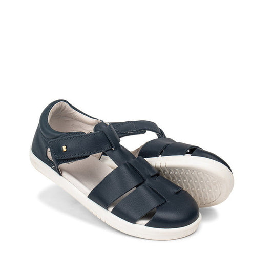 The Bobux Kid+ Tidal Closed Toe Quick Dry Sandal Navy (834404A) features navy blue leather, white rubber soles, and adjustable velcro straps. One sandal is positioned slightly ahead of the other in the image.