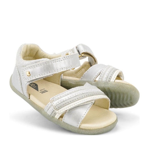 The Bobux Step Up Magic Leather Toddlers Sandal in silver features open toes, adjustable Velcro straps, and cushioned beige soles—ideal as a first walker—shown against a white background.