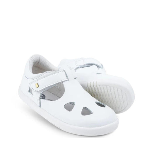 The Bobux IWalk IW Zap II Closed Toe Sandal in white features a children's leather upper with front cut-out shapes, closed-toe design, Velcro straps, and textured rubber soles. One sandal stands upright, the other shows the sole laid on its side.
