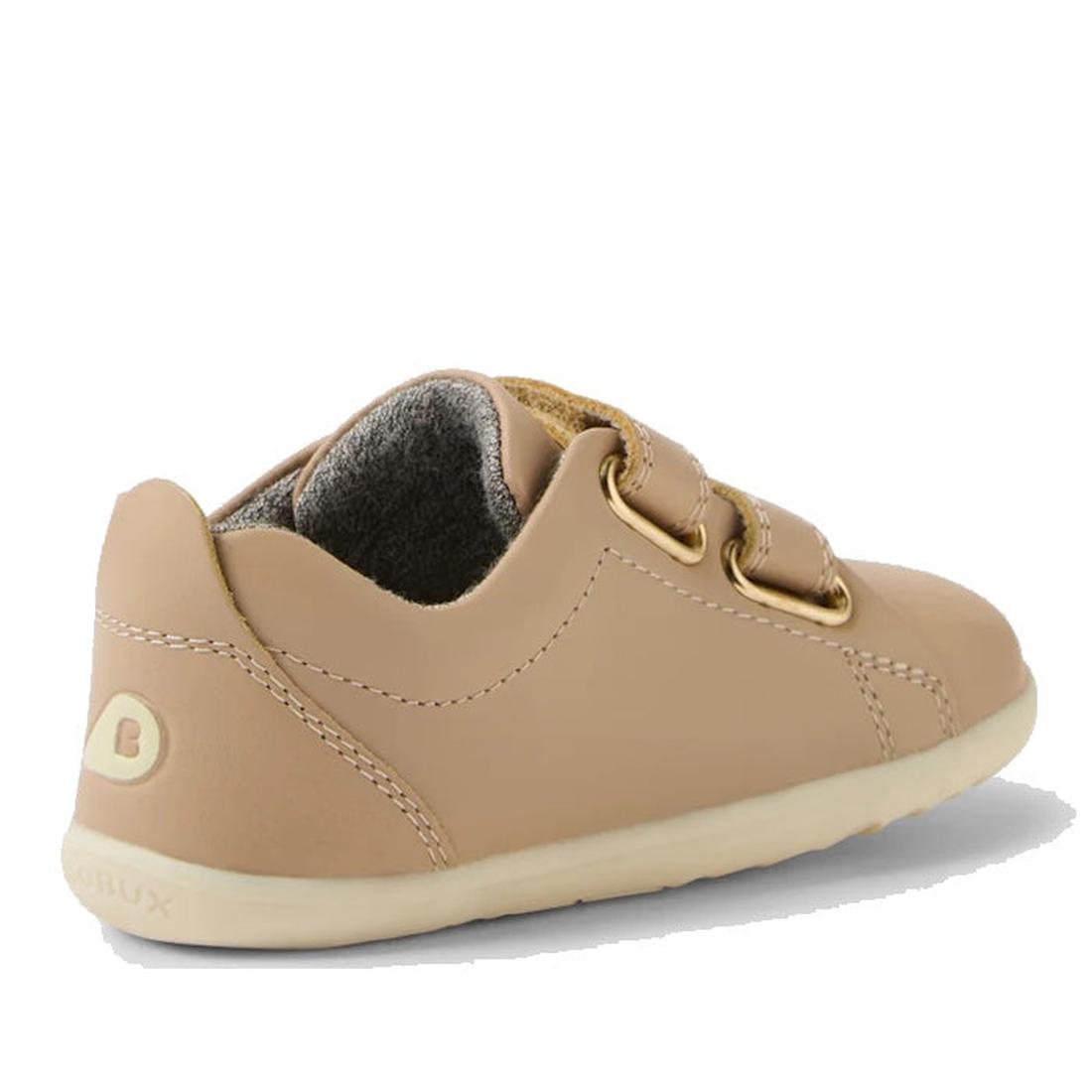 The Bobux Step Up Grass Court Trainer Warm Taupe Shoes are tan leather toddler sneakers with beige soles, gold eyelets, tan laces, visible stitching, a soft gray lining, and a B logo—ideal first walker shoes for stylish little ones., 9420074802033, 942007