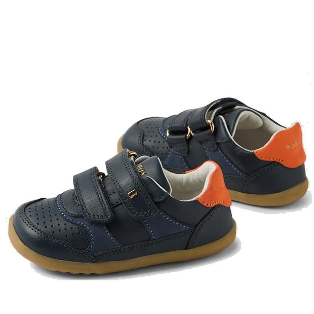 The Bobux SU Step Up Hunter Leather Toddlers Sneaker in navy features orange heel accents, tan rubber soles, double Velcro straps, perforated toe detailing, and the BOAR brand on the straps and heel—perfect for first walkers.