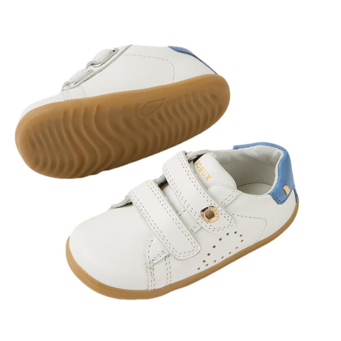 The Bobux SU Step Up Maverick Leather Toddlers Sneaker in White Coronet Blue features white leather, blue heel accents, light brown soles, and two velcro straps—perfect breathable first walker shoes for toddlers. One shoe shown from the side, one sole vie