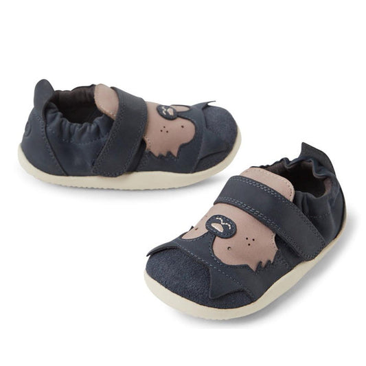 The Bobux XP Xplorer Howl First Walking Shoes in navy feature light brown bear face designs on the toes and an adjustable strap, displayed against a white background.