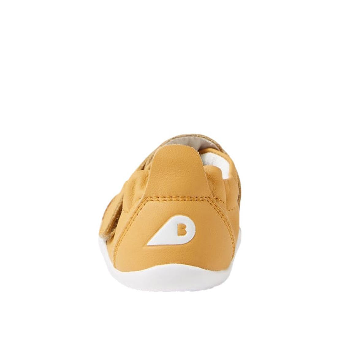 The Bobux XP Xplorer First Walking Shoes Go Oak Buff Tan are tan pre-walker leather shoes seen from the back, with a flexible white sole and a white triangle B logo on the heel, set against a plain white background., 9420068567962, 9420068567979, 94200685