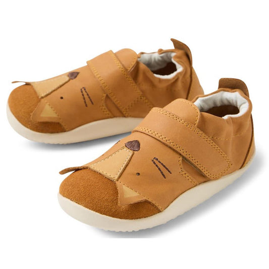 The Bobux XP Xplorer Rummage First Walking Shoes in Pumpkin Spice Orange feature velcro straps, a cute lion face with ear and nose details, and white flexible EVA soles. Perfect pre-walker shoes for little adventurers.