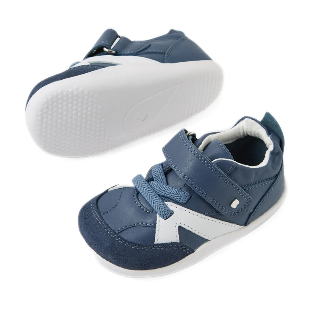 A pair of Bobux Xplorer XP Chase Vintage Indigo Blue First Walker Crawlers, featuring blue and white design with white rubber soles—one shoe upright and the other displaying its textured sole—complete with laces and a hook-and-loop strap, perfect for your