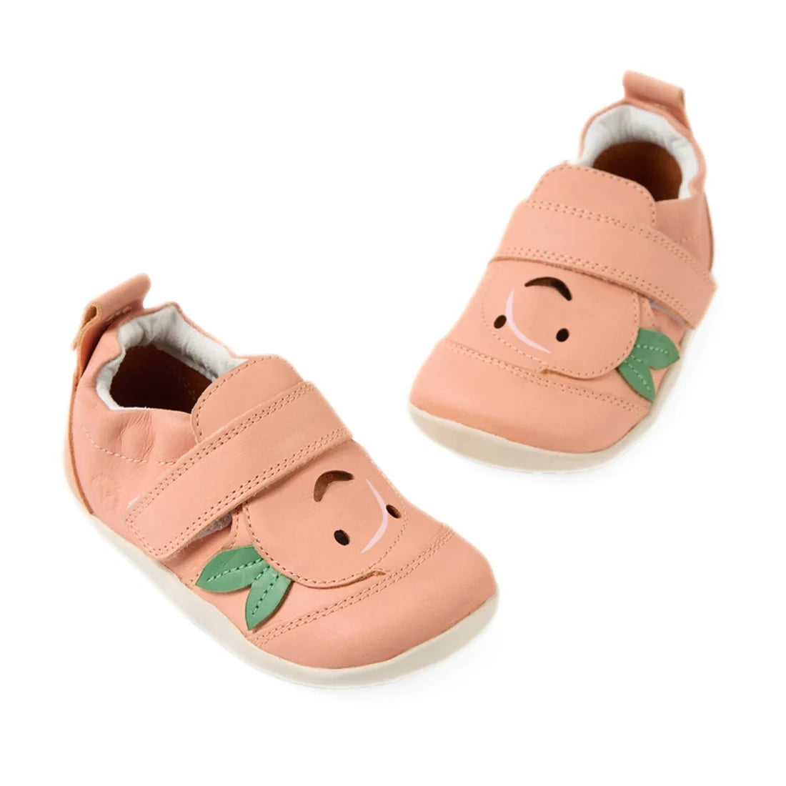Bobux XP Explorer Little Sprouts Peach Pop First Walker Pink shoes feature a peach-colored design with velcro straps, decorated with smiling peach faces and green leaves on the front, set against a white background.
