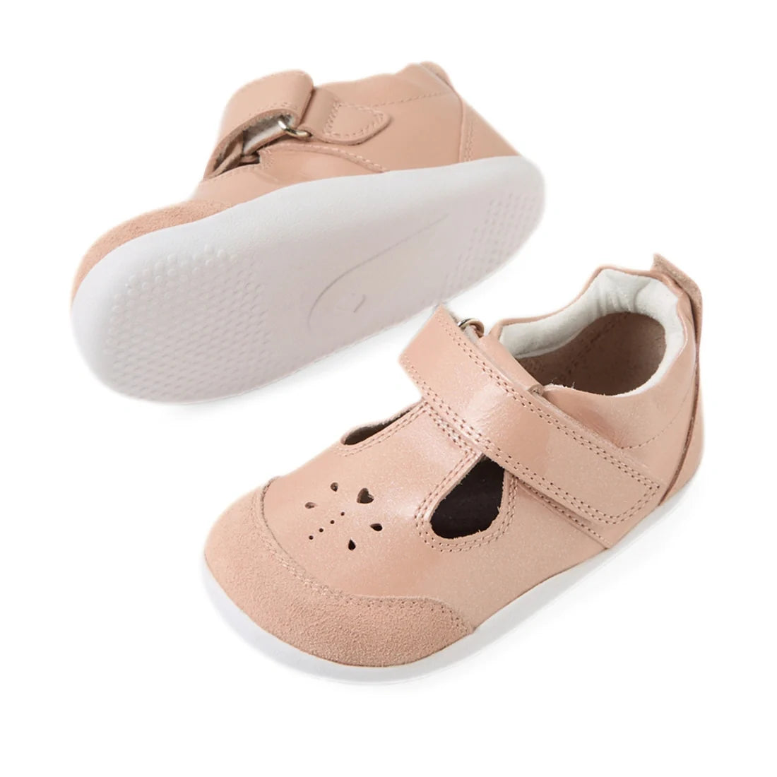 Introducing the Bobux XP Explorer Rue First Walker Sandal Camo Rose Pink—a pair of light pink leather T-bar shoes featuring white flexible soles, Velcro straps, and charming heart-shaped cutouts on the toe area. One sandal stands upright while the other i