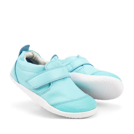 The Bobux Xplorer Go Aqua First Walker Crawler is a pair of light blue baby walking shoes with premium soft leather, white Velcro straps, and a flexible sole, shown on a white background.