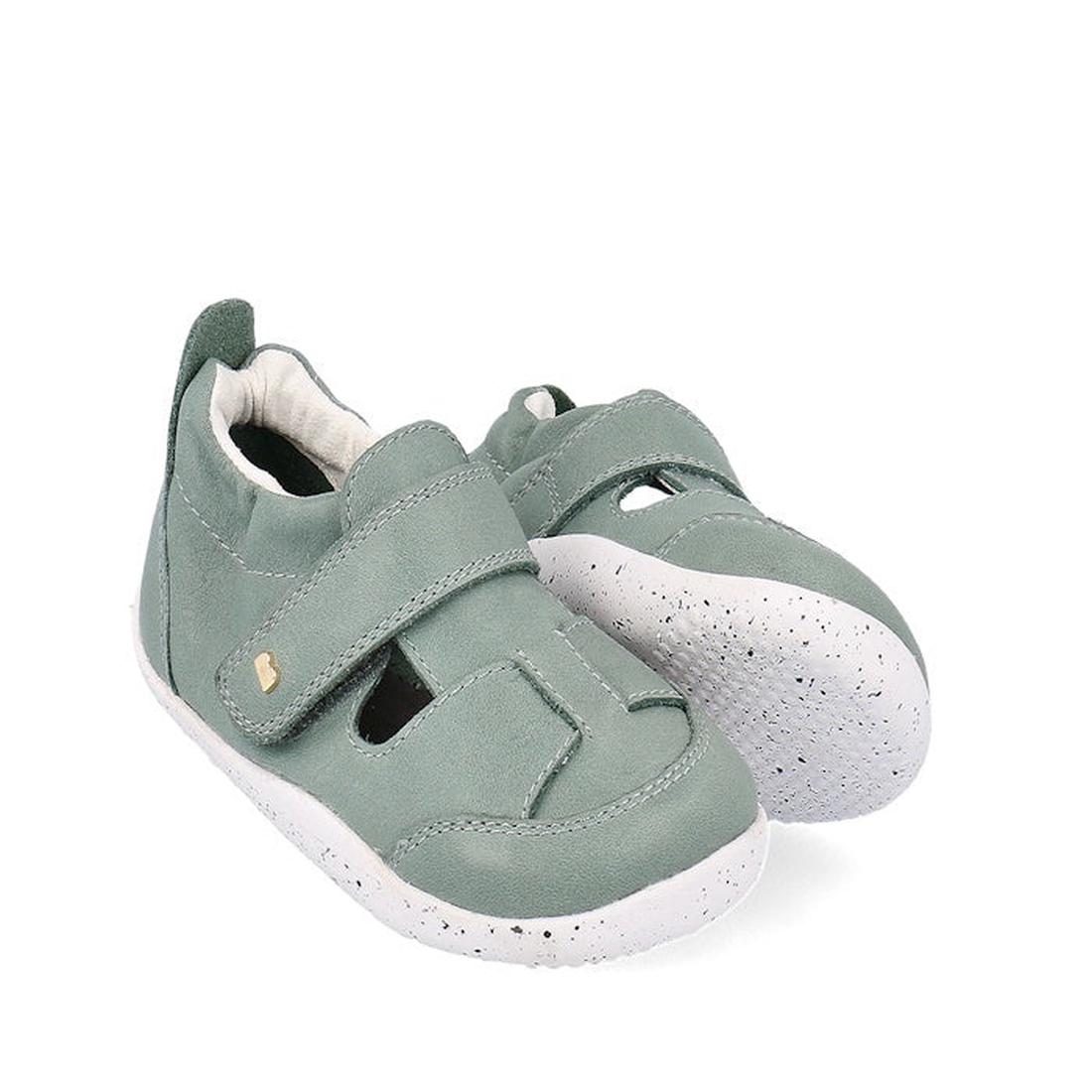 The Bobux XP Explorer Beau First Walker Sandal in Sage Green (502304) features white speckled rubber soles, velcro straps, and a gold accent, offering comfort and support for toddlers learning to walk. Shown on a white background.