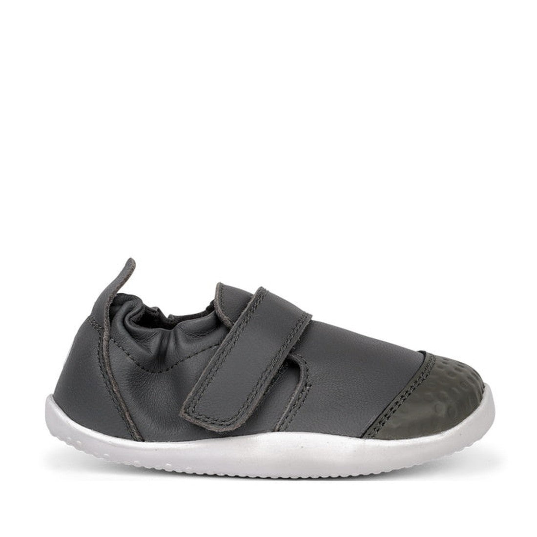 The Bobux Xplorer XP Go Smoke Grey First Walker Crawler 501002B is a dark gray children's shoe with a white flexible sole, velcro strap, and reinforced toe cap, made from premium soft leather and shown in profile against a white background., 9420062079744