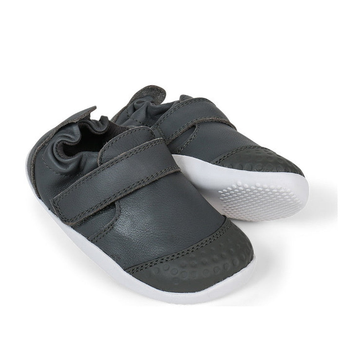 The Bobux Xplorer XP Go Smoke Grey First Walker Crawler 501002B features premium soft leather in dark gray with white rubber soles, a textured toe, and adjustable Velcro straps—ideal first walking shoes for babies, displayed against a white background.